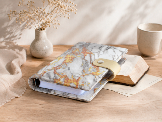 Marble-patterned notebook on a wooden surface with a vase and cup in the background