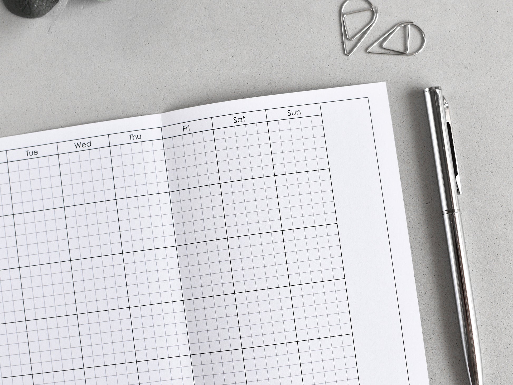 Weekly planner with grid layout on a gray surface with a pen and paper clips.