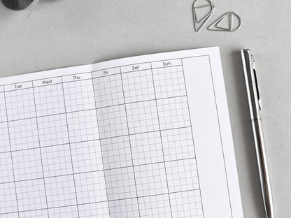 Weekly planner with grid layout on a gray surface with a pen and paper clips.