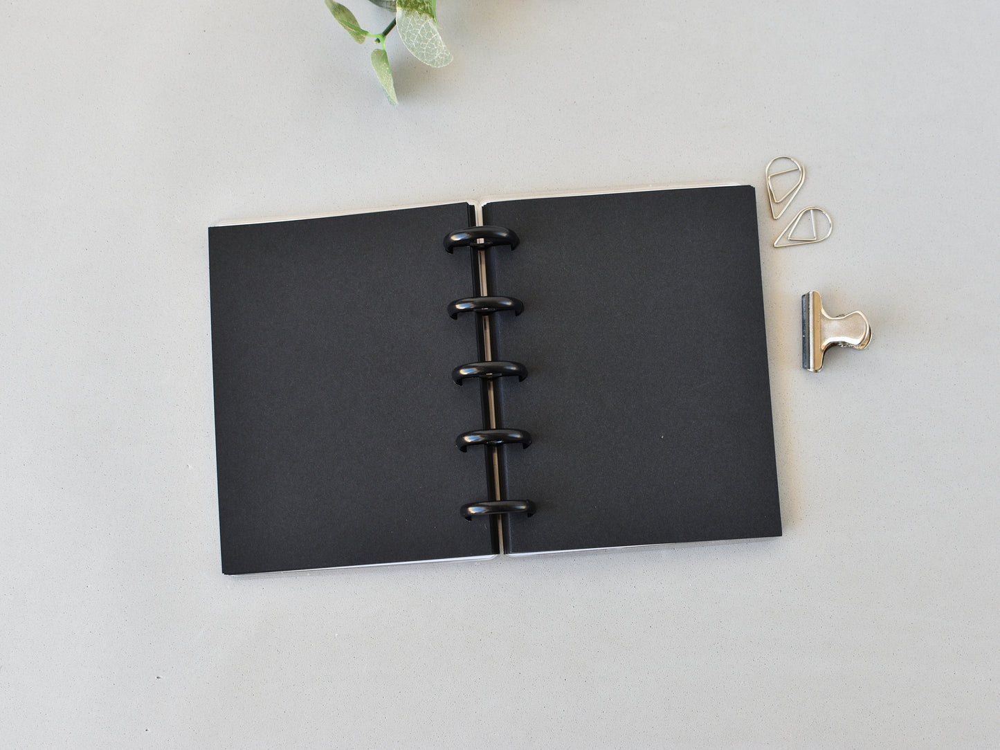Black disc-bound notebook on a light gray surface with decorative clips.
