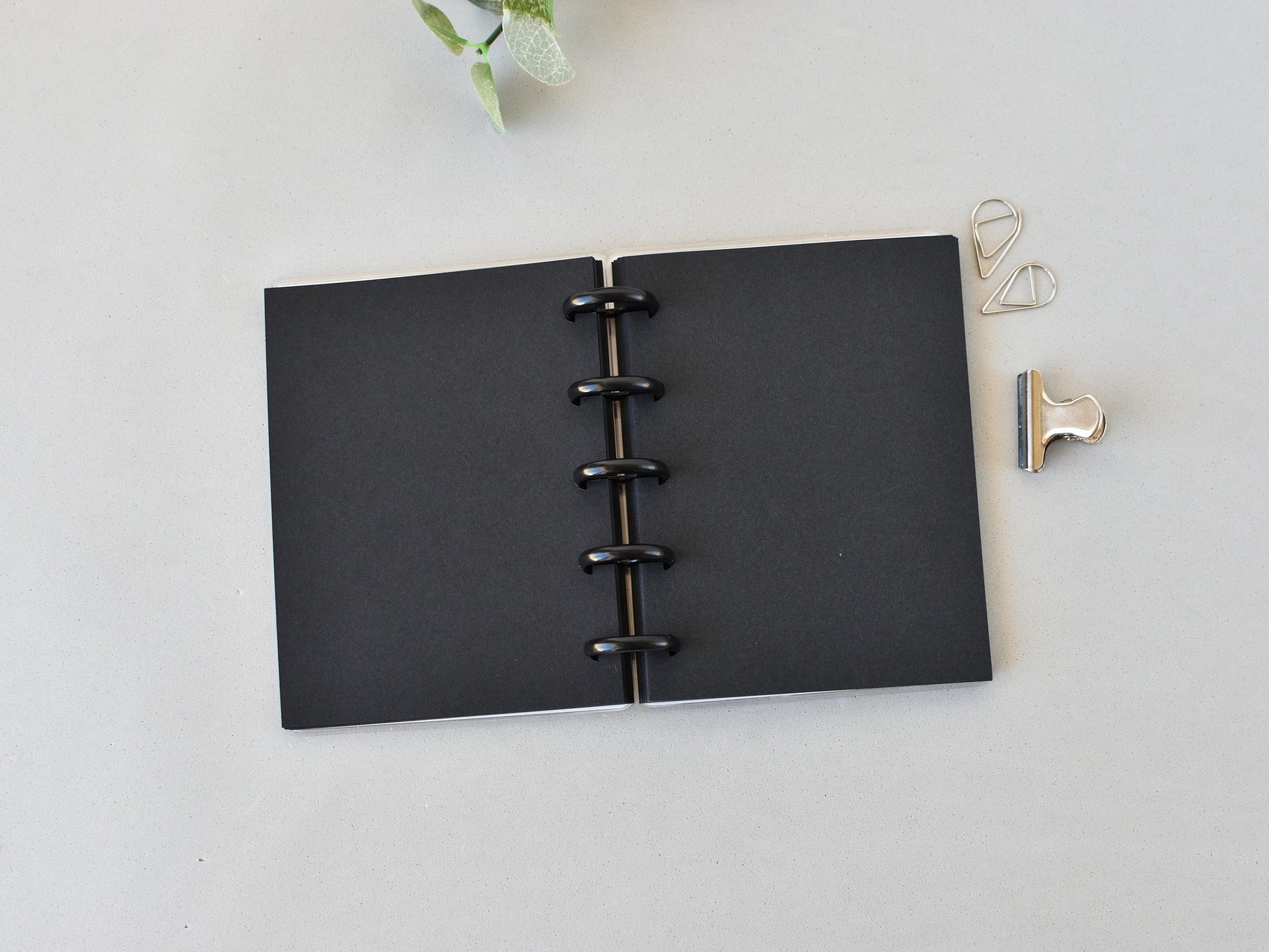 Black disc-bound notebook on a light gray surface with decorative clips.
