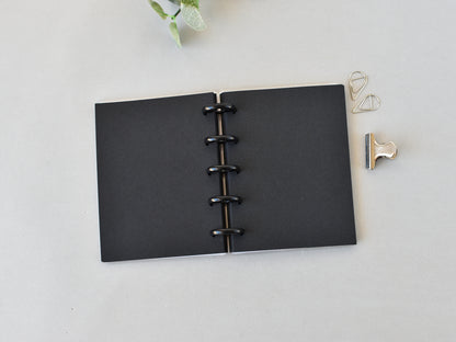 Black disc-bound notebook on a light gray surface with decorative clips.
