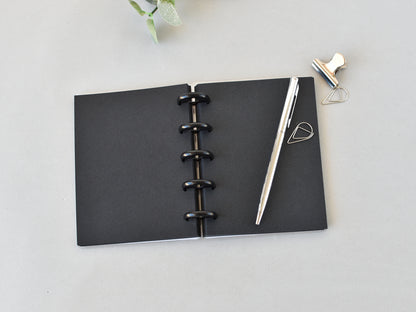 Black pages notebook with a pen on a light gray surface