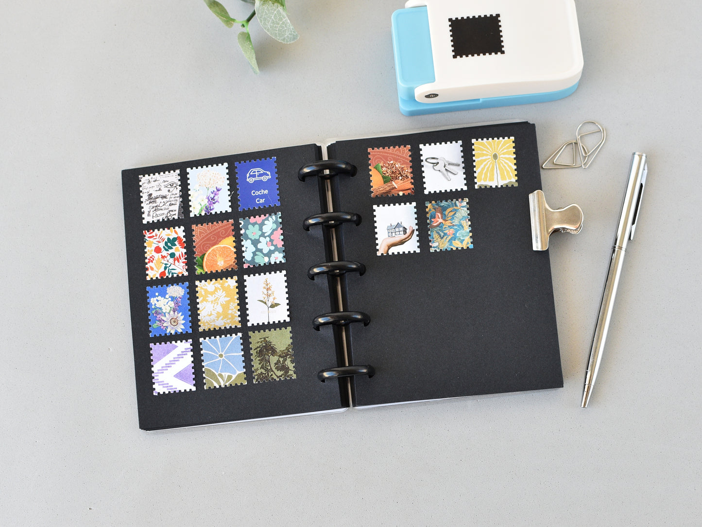 Black discbound notebook with colorful stamp designs on a light gray surface.